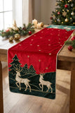 Runner natalizio Deer Clodette rosso con cervi, abeti verdi e stelle, steso su una tavola in legno.