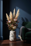 Vaso decorativo a terra in angolo con fondo scuro e composizione verticale di fiori secchi